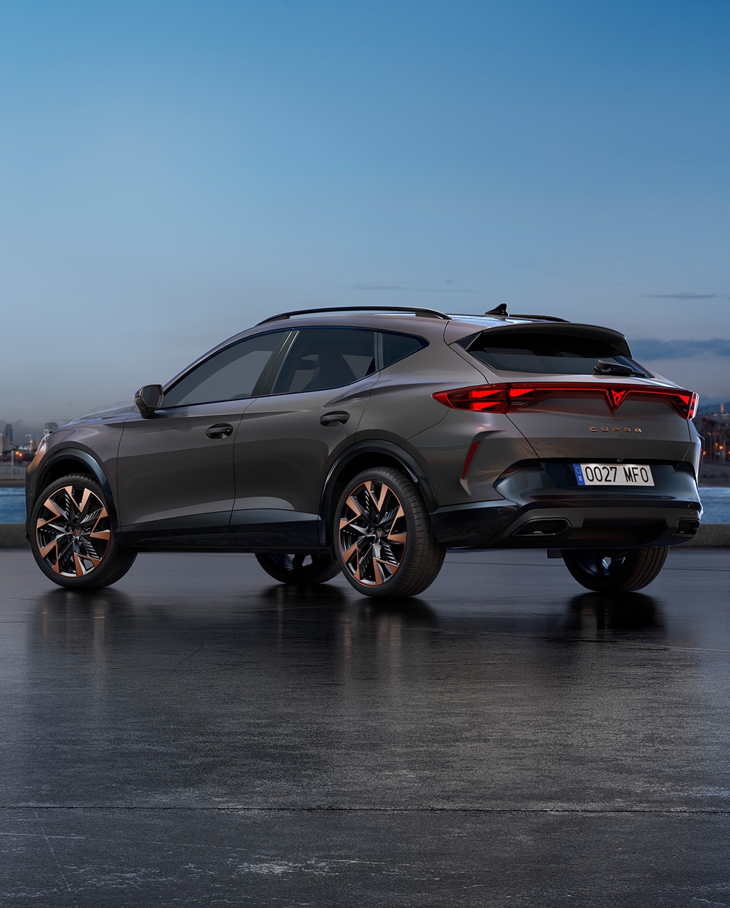 A new CUPRA Formentor 2025 graphene grey CUV parked on a waterfront promenade during twilight. The background features a cityscape with skyscrapers and palm trees illuminated by the fading light of the day.