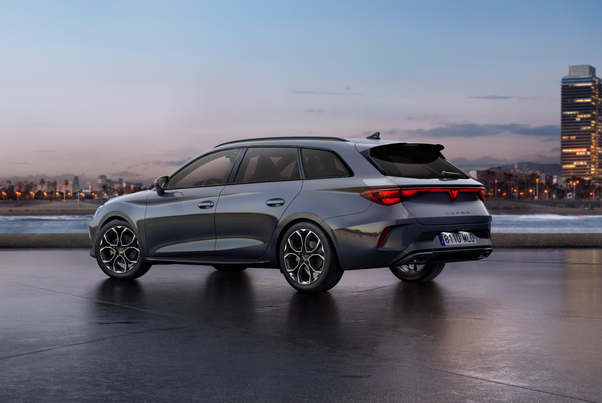 Rear view shot of new Cupra Leon Sportstourer 2025 glossy grey car model with dynamic chassis control, plus black and copper alloy wheels. City in the background at sunset.