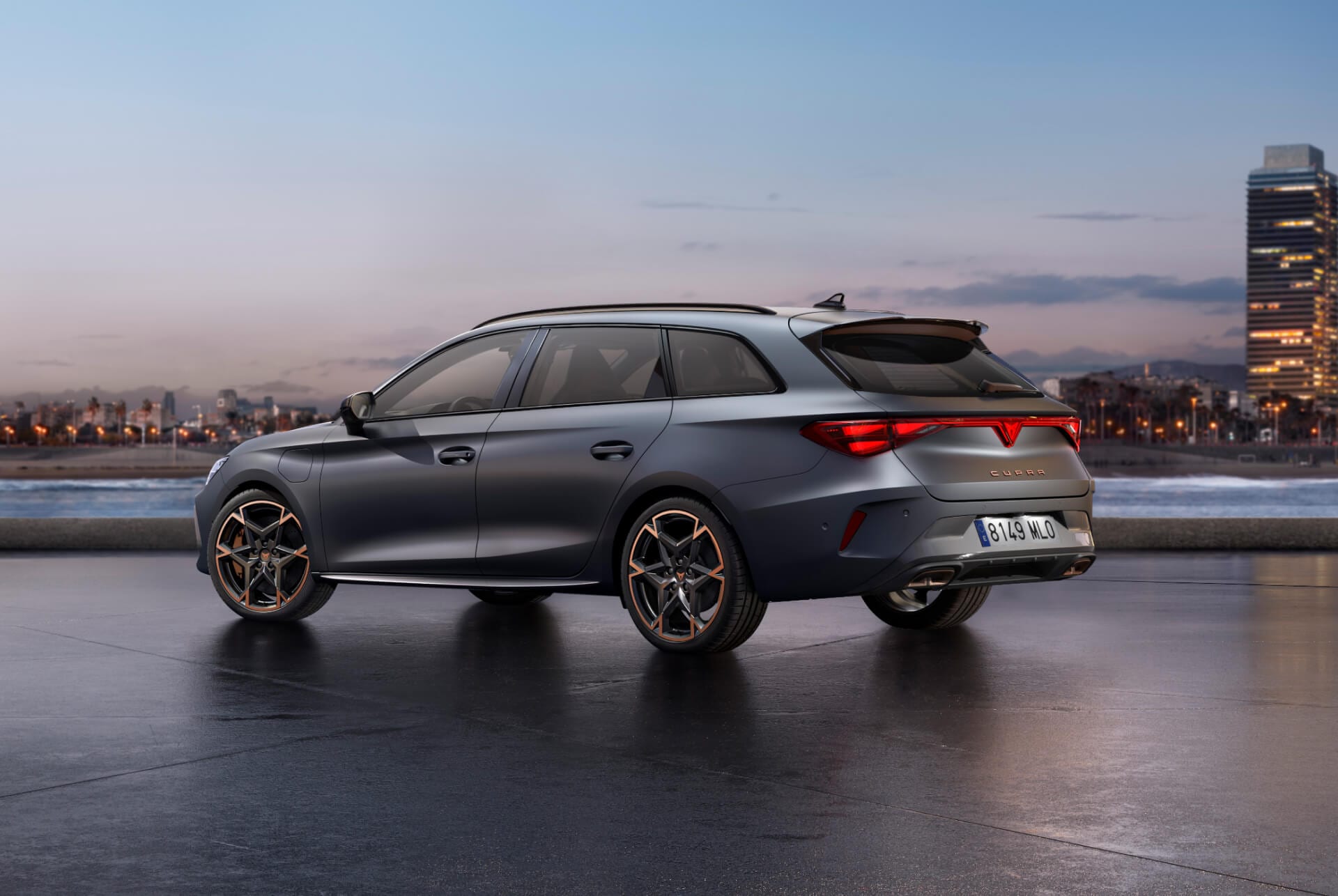The sporty new 2025 Cupra Leon Sportstourer parked on concrete with a city skyline illuminated at twilight in the background. The vehicle is depicted in a matte grey finish.